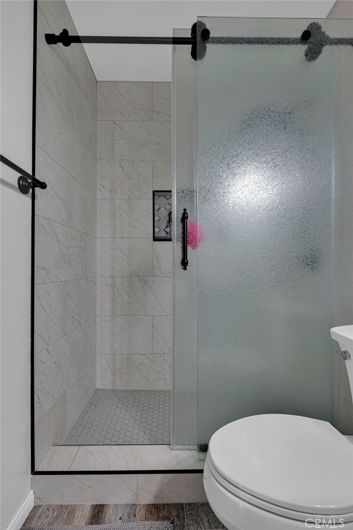 Bathroom with a frosted-glass shower, marble-look tile, black hardware, and a partially visible toilet.