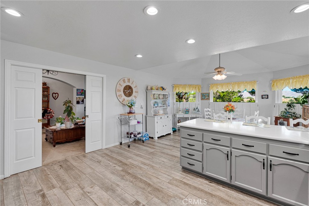 Bright kitchen with a large white island, gray cabinetry, plank-style flooring, and curtained windows.