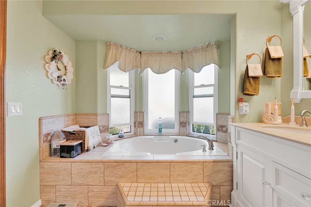 Bathroom with a tiled soaking tub beneath three tall windows and a white vanity.