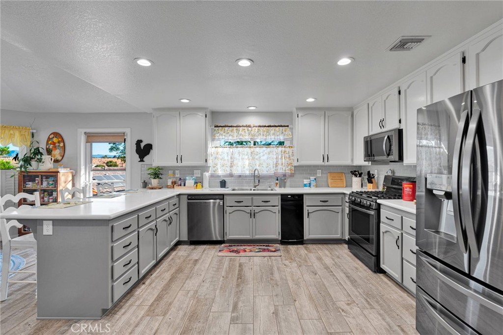 Kitchen with white cabinets, a large peninsula, stainless steel appliances, and wood-look tile flooring.
