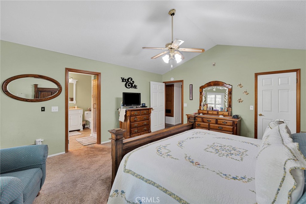 Furnished bedroom with a large bed, wood dressers, and an open doorway to the bathroom.