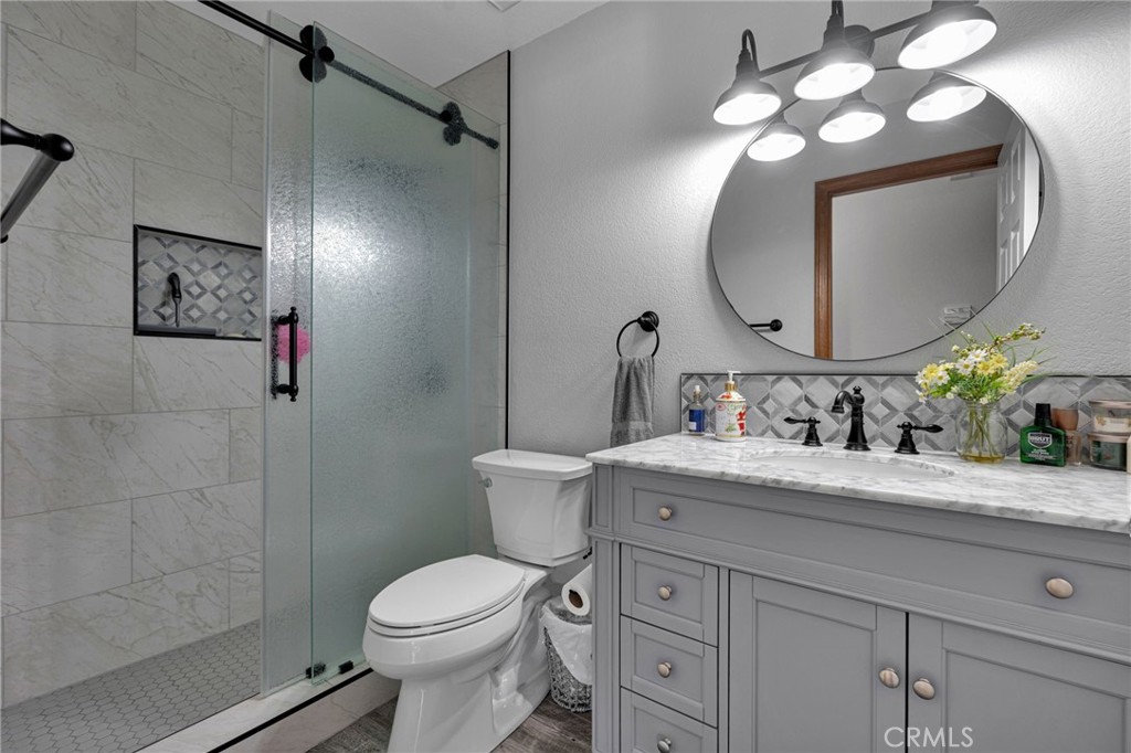 Bathroom with a glass shower, marble-look tile, and gray vanity beneath an oval mirror.