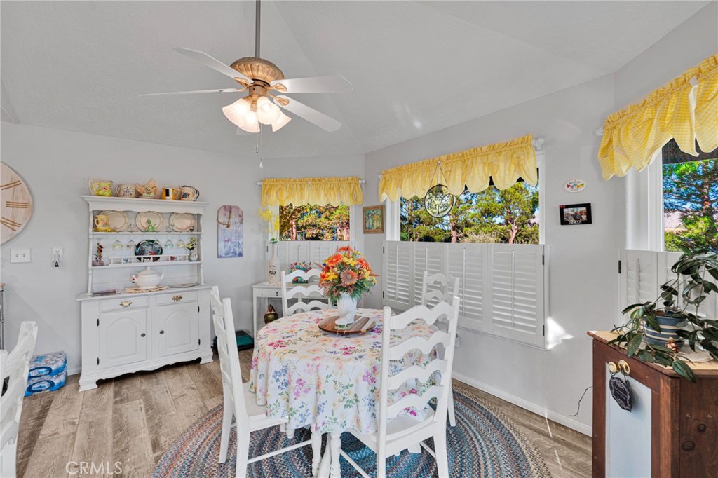 Dining room with a floral tablecloth, white china hutch, yellow valances, and plantation shutters.