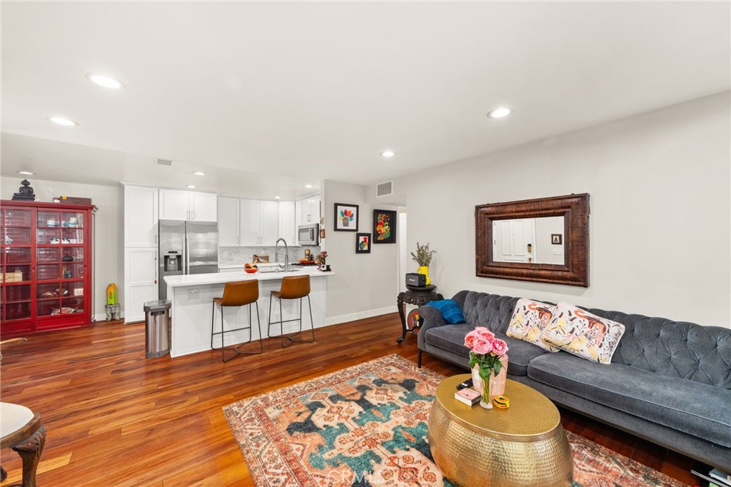 Open-plan living room and kitchen with a gray tufted sofa, white cabinets, and hardwood floors.