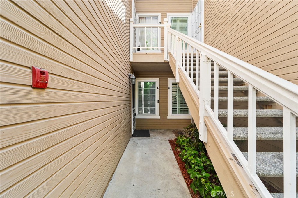 Residential entry walkway with tan siding, white-railed stairs, and plants beside the concrete path.