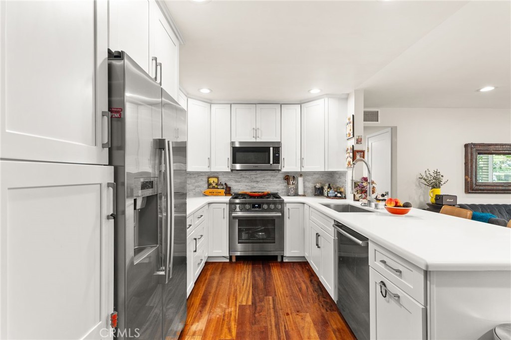 Kitchen with white cabinets, stainless steel appliances, a large peninsula, and warm hardwood floors.