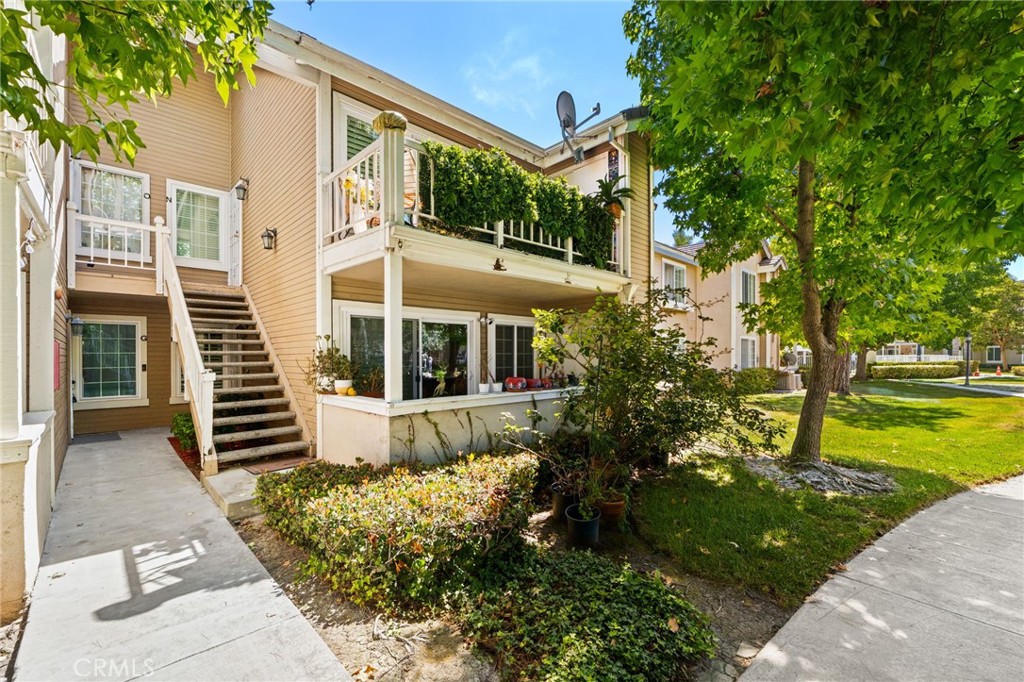 Multi-unit residential building with two balconies, exterior stairs, and leafy landscaping.