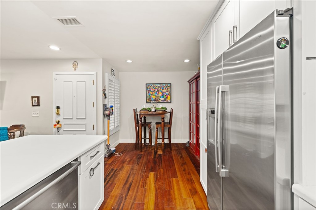 Kitchen with stainless steel refrigerator, white cabinetry, and a small dining table on wood floors.