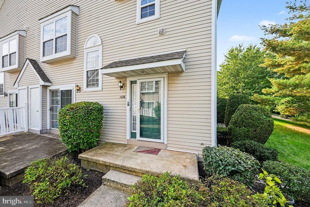 Townhouse entrance with a teal front door, covered stoop, and landscaped shrubs.