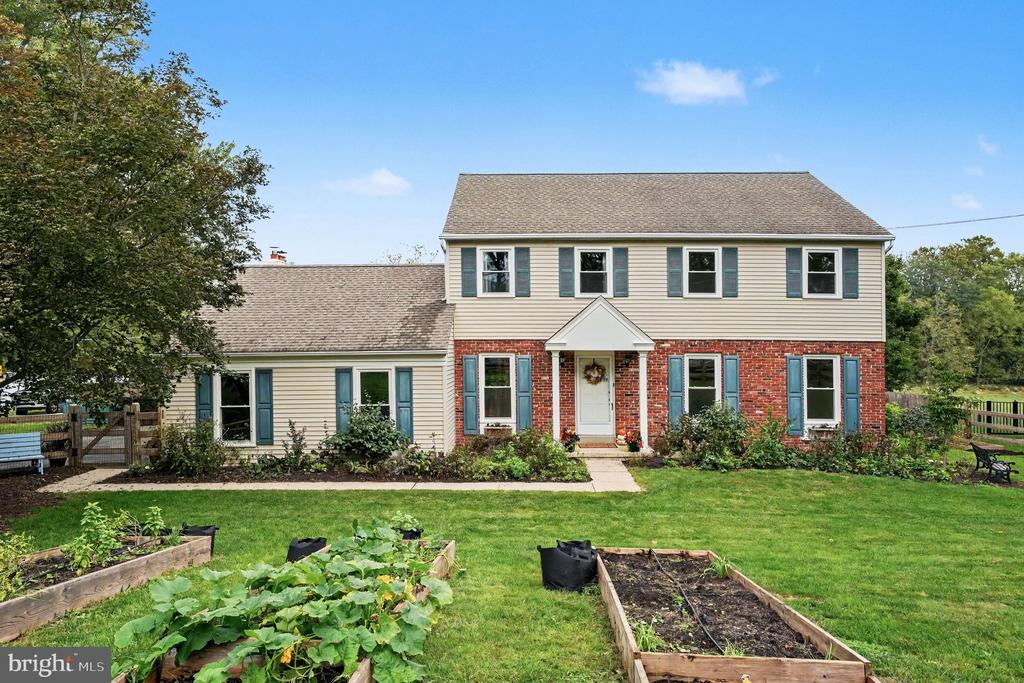 Two-story home with red brick and siding, blue shutters, and raised garden beds.
