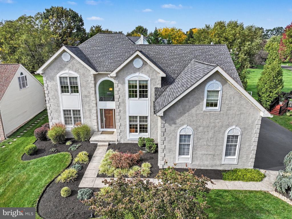 Gray stone two-story home with multiple gables, landscaped front garden, and paved driveway.