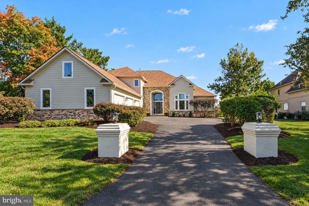 Large home with gray siding and stone accents at the end of a landscaped driveway.