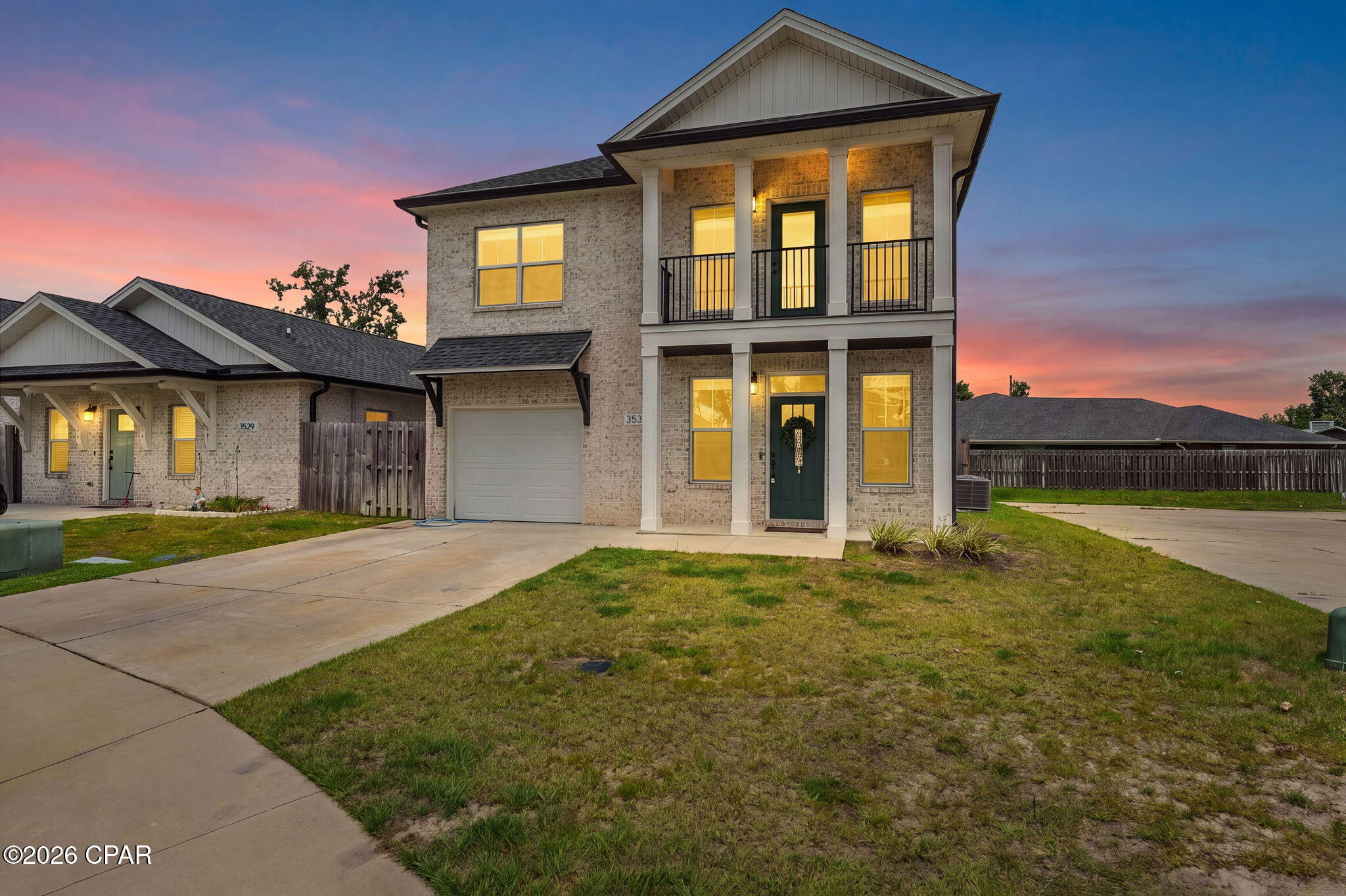 Two-story brick home with a covered balcony and glowing windows at dusk.