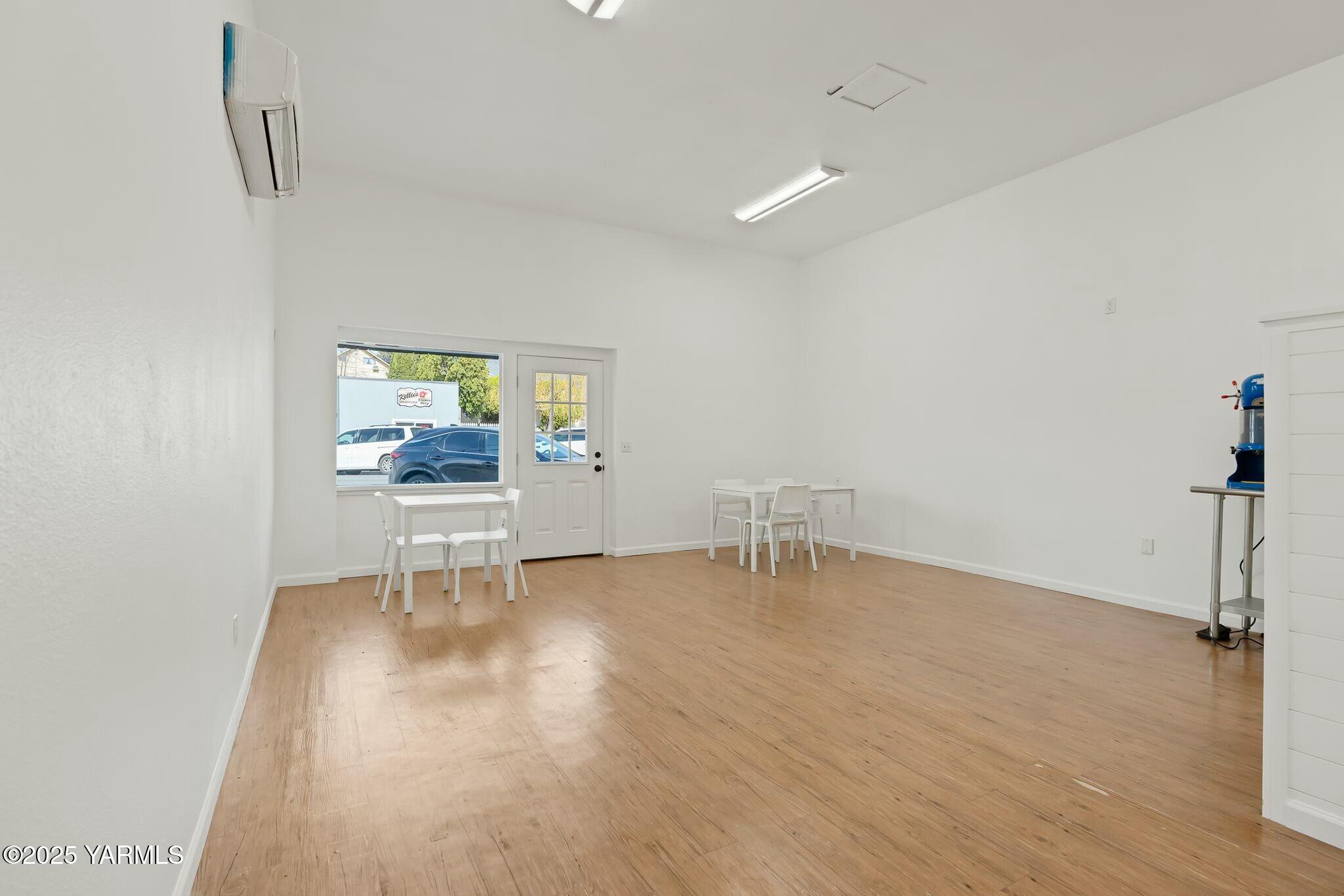 Bright commercial interior with light wood flooring, two small tables, and a street-facing window.