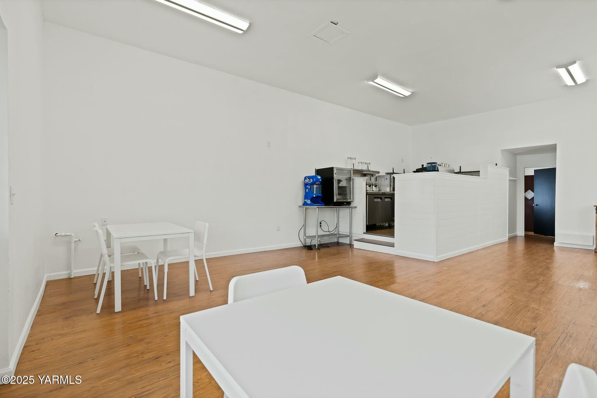 Open commercial interior with wood floors, white tables, and a service counter with beverage equipment.