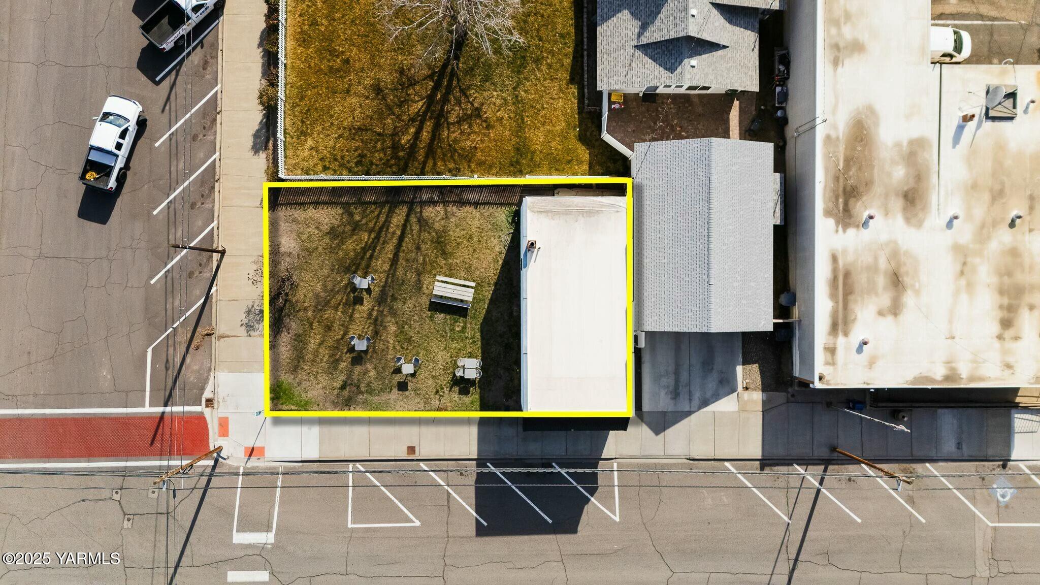 Aerial view of the property lot outlined in yellow, with a fenced yard and adjacent building.