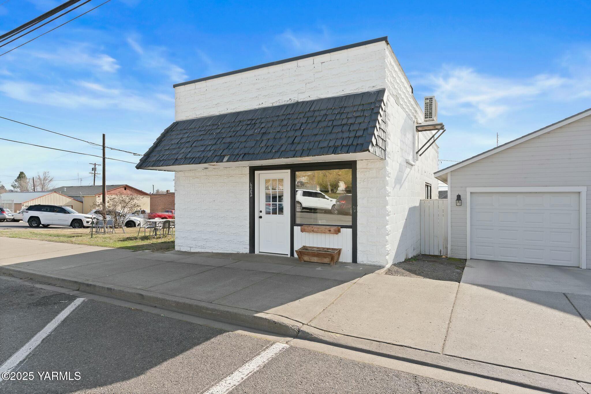 White masonry storefront with a dark shingled awning and glass-front entry beside a garage.