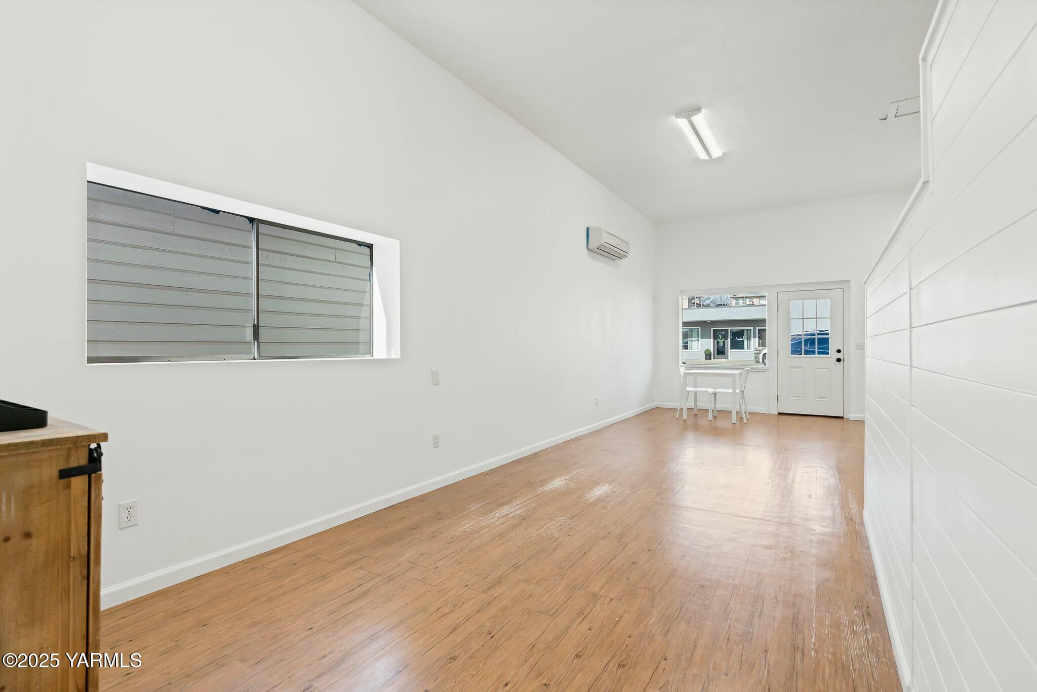Long, narrow room with wood-look flooring, a large interior window, and a glass-paneled entry door.