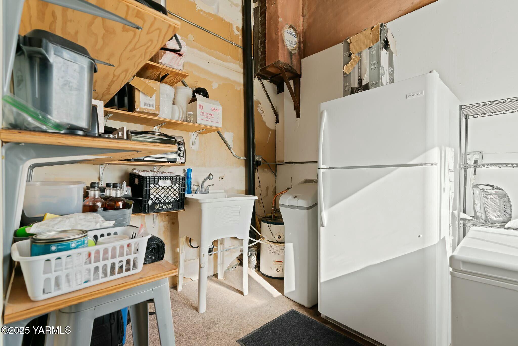 Laundry room with washer and dryer, utility sink, refrigerator, and crowded storage shelves.