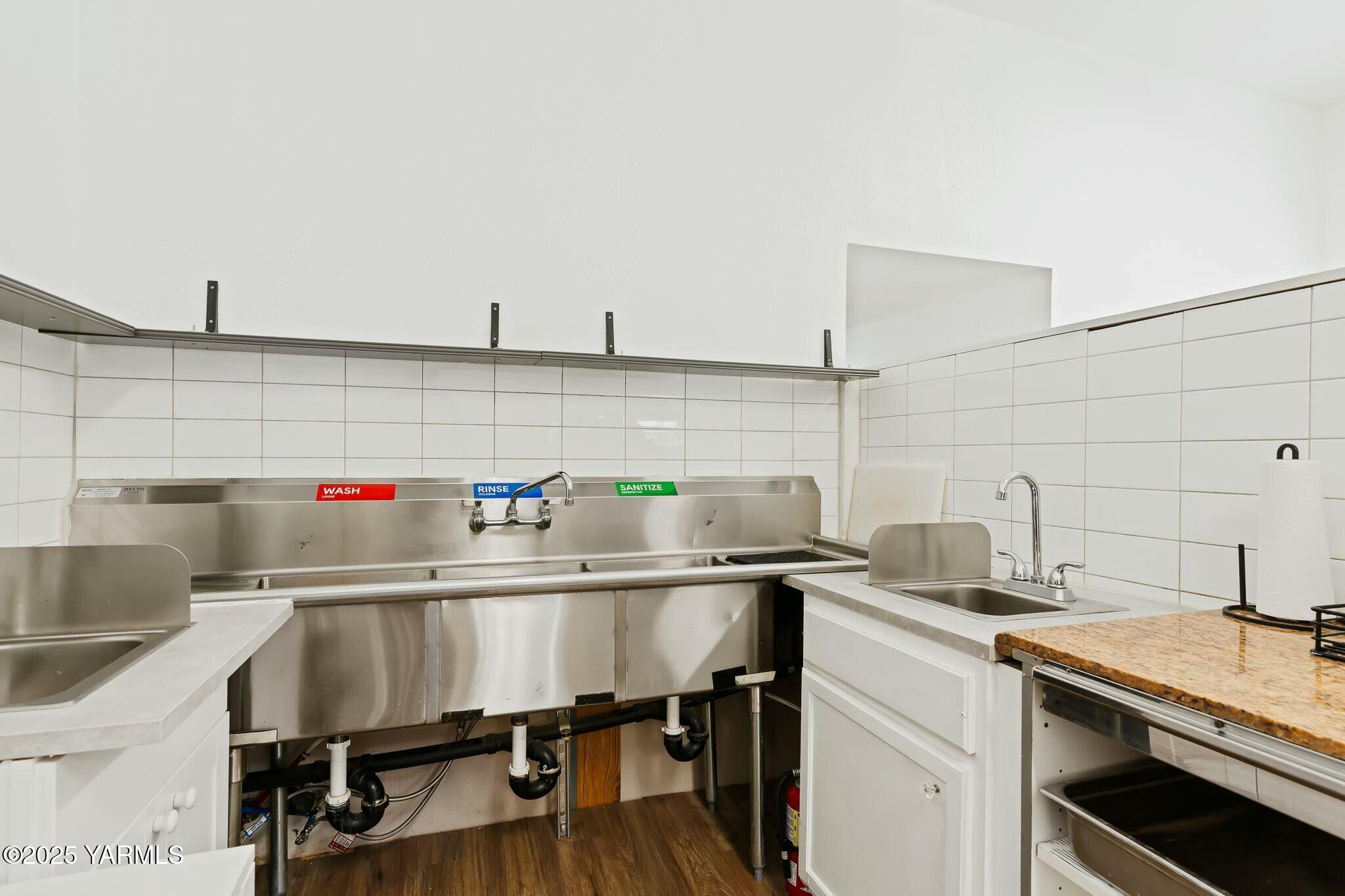 Commercial kitchen with a stainless wash-rinse-sanitize sink station and white tiled walls.