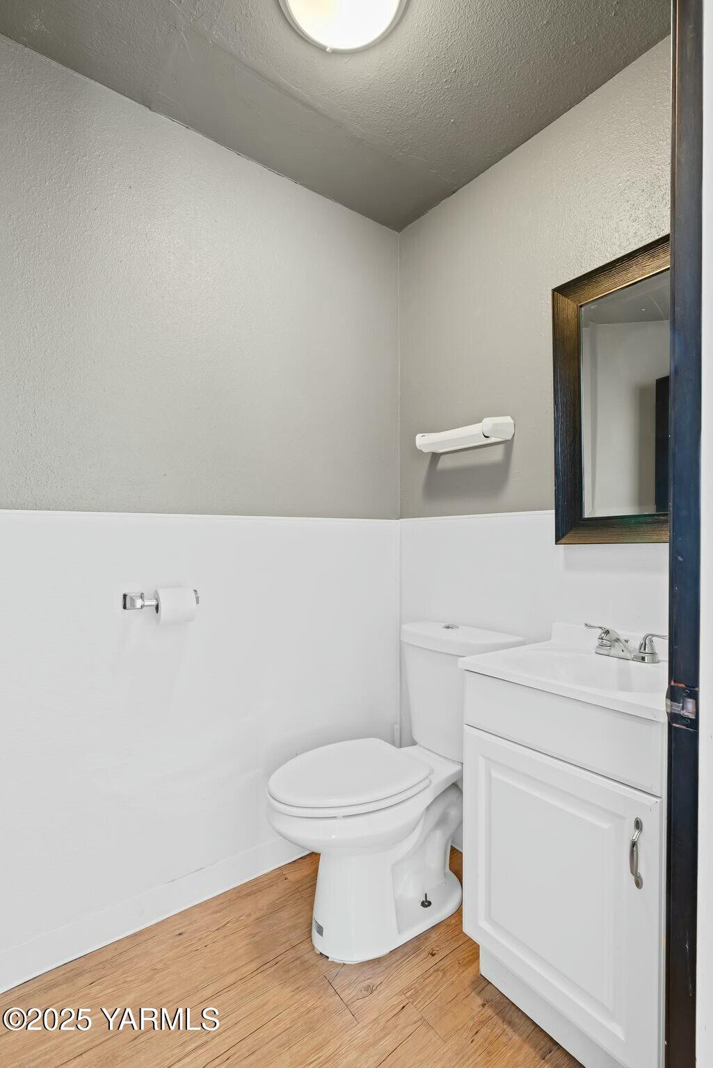 Bathroom with a white toilet and vanity, dark-framed mirror, and wood-look floor.