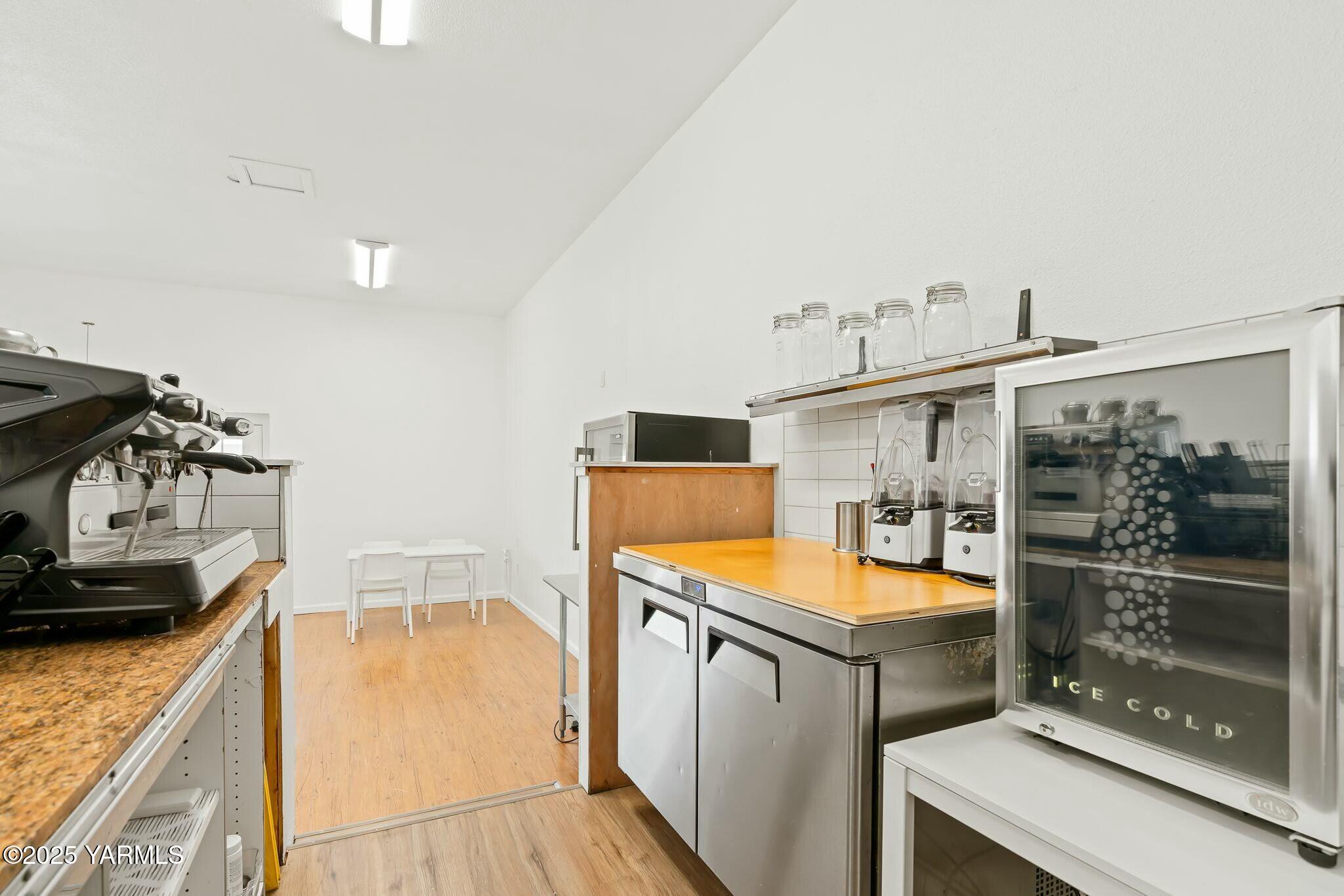 Commercial café kitchen with an espresso machine, grinders, and glass-front beverage cooler.