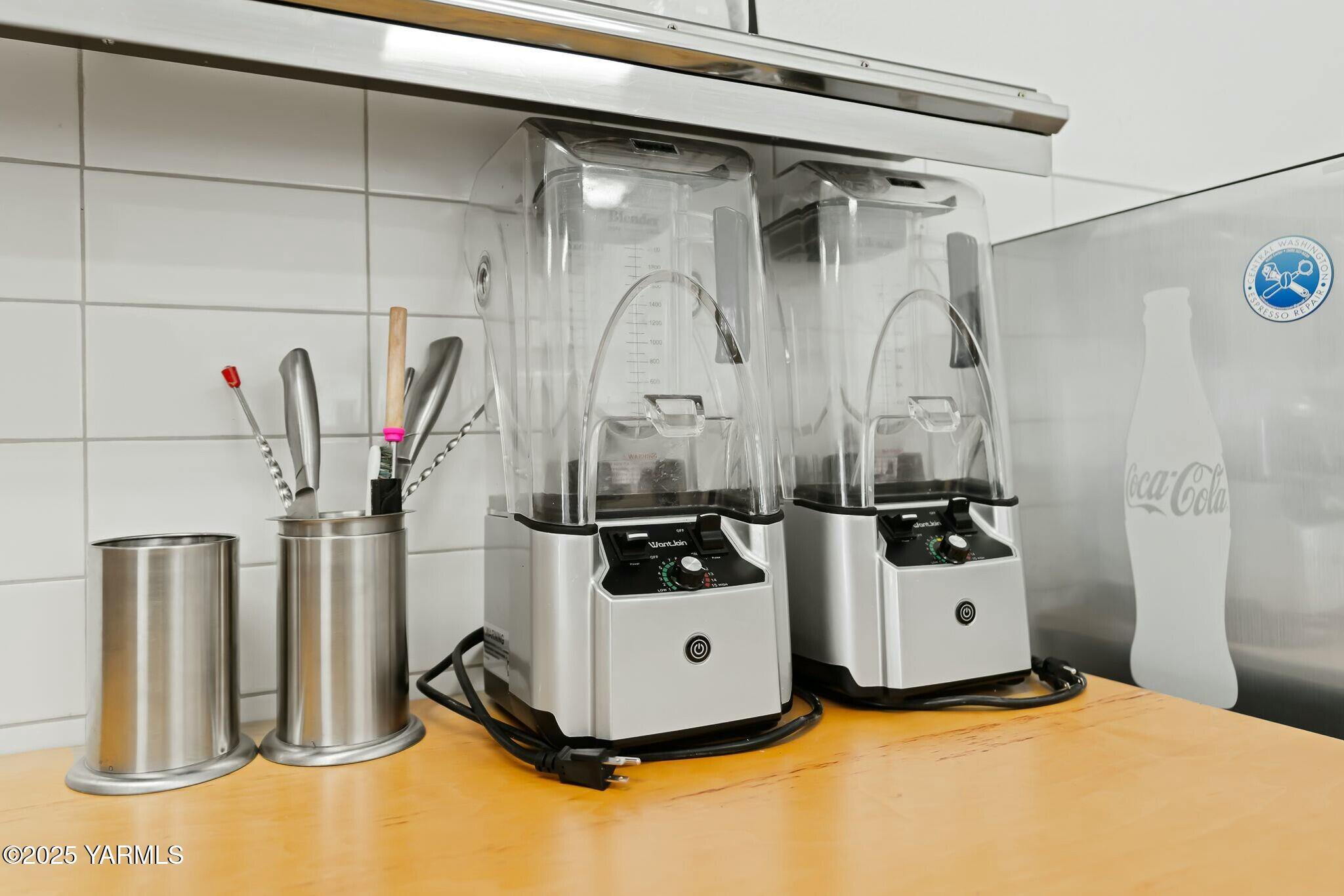 Kitchen counter with two commercial blenders and stainless-steel utensil holders.
