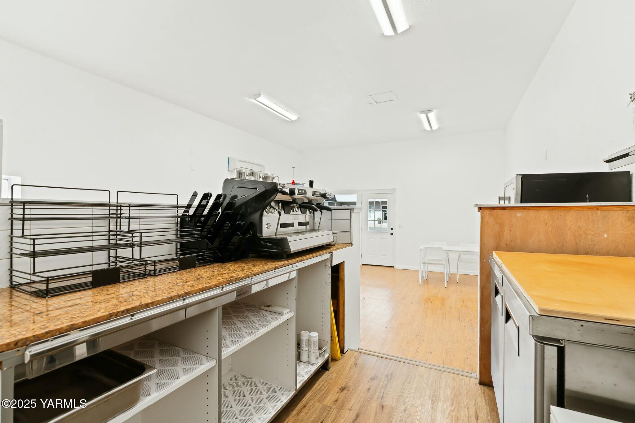 Commercial kitchen with an espresso machine, metal dish racks, granite counter, and wood-fronted work area.