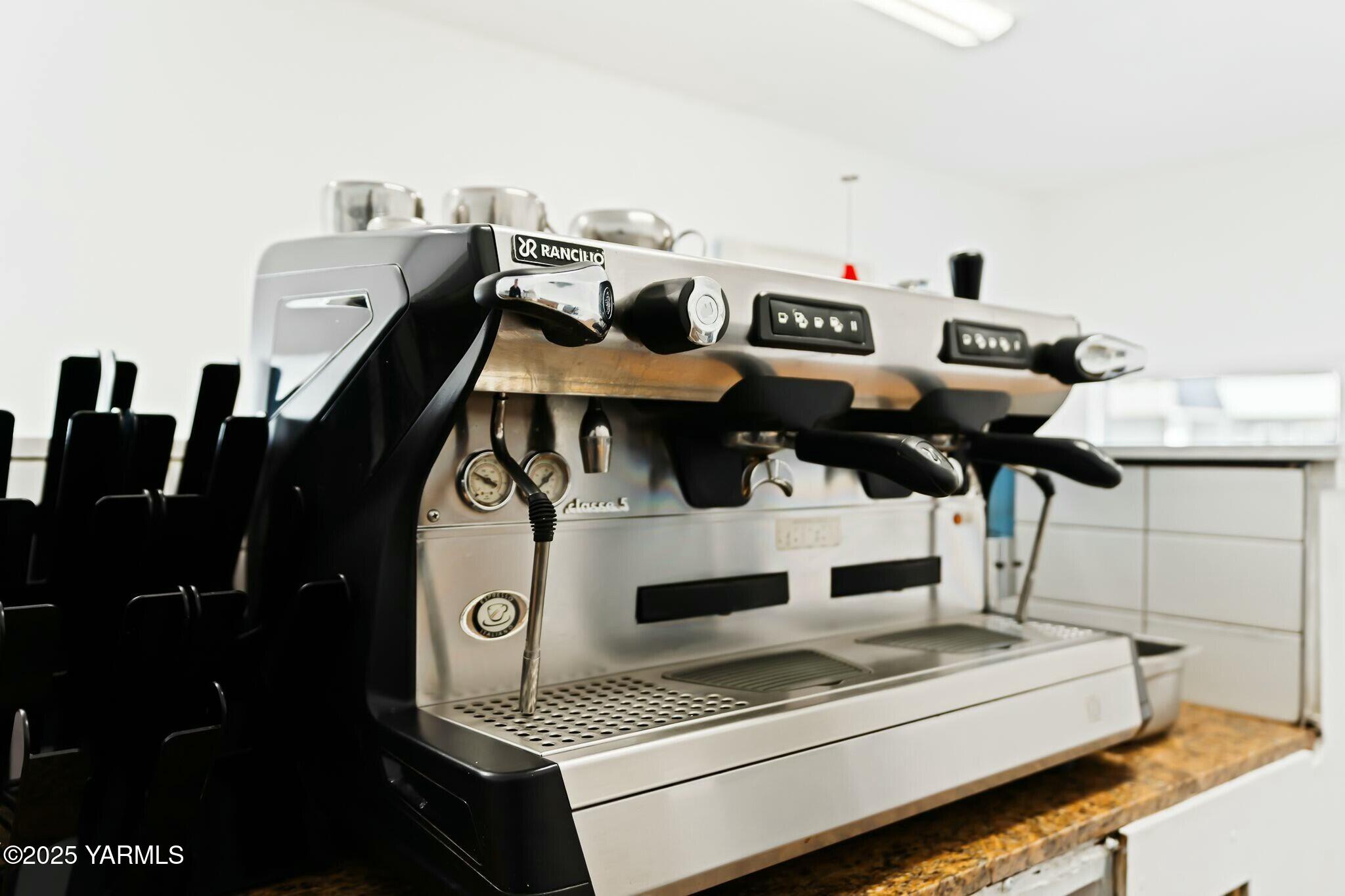 Commercial espresso machine with multiple group heads and steam wand on a granite counter.