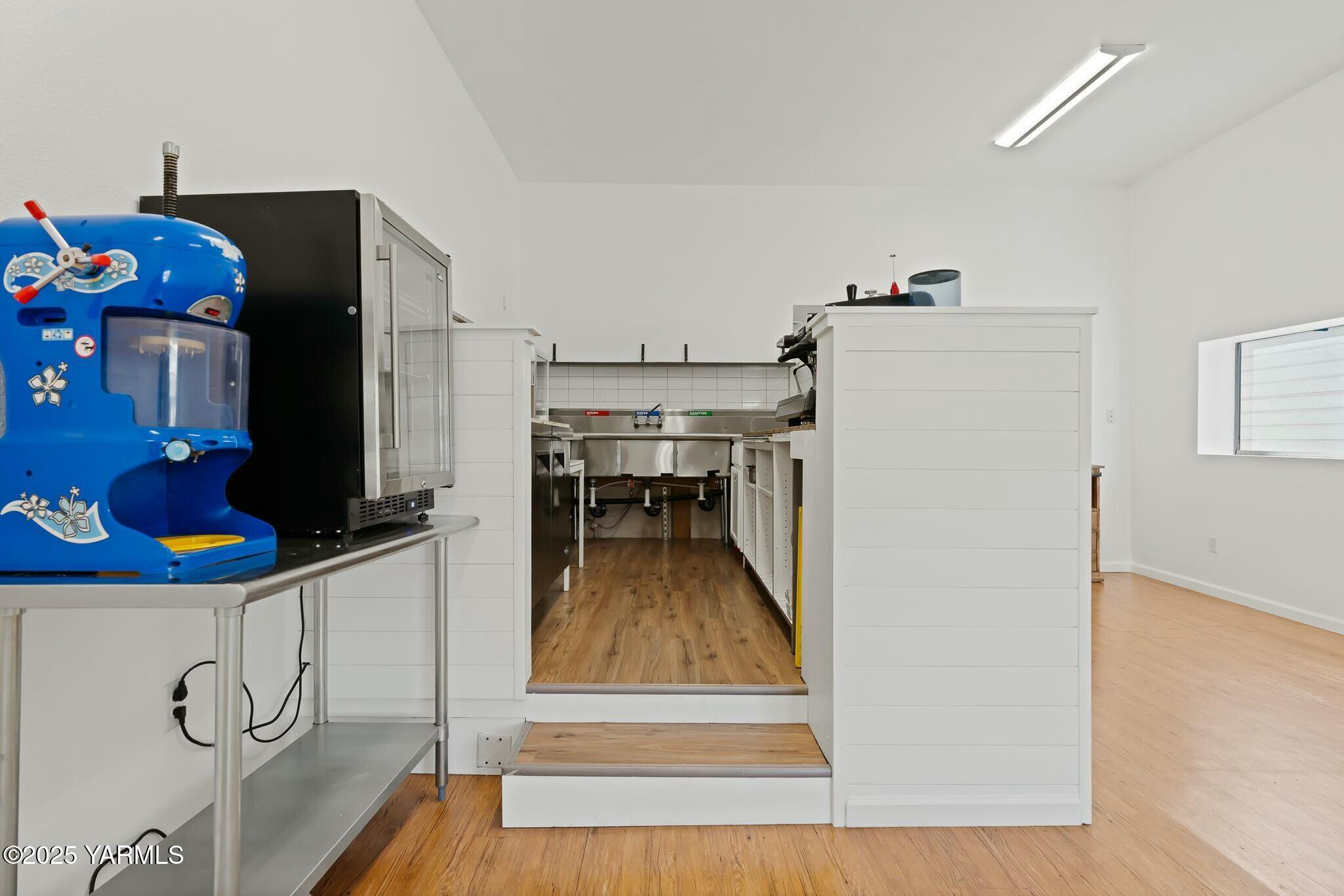 Commercial kitchen with stainless-steel prep sink, refrigeration units, and a prominent blue countertop machine.