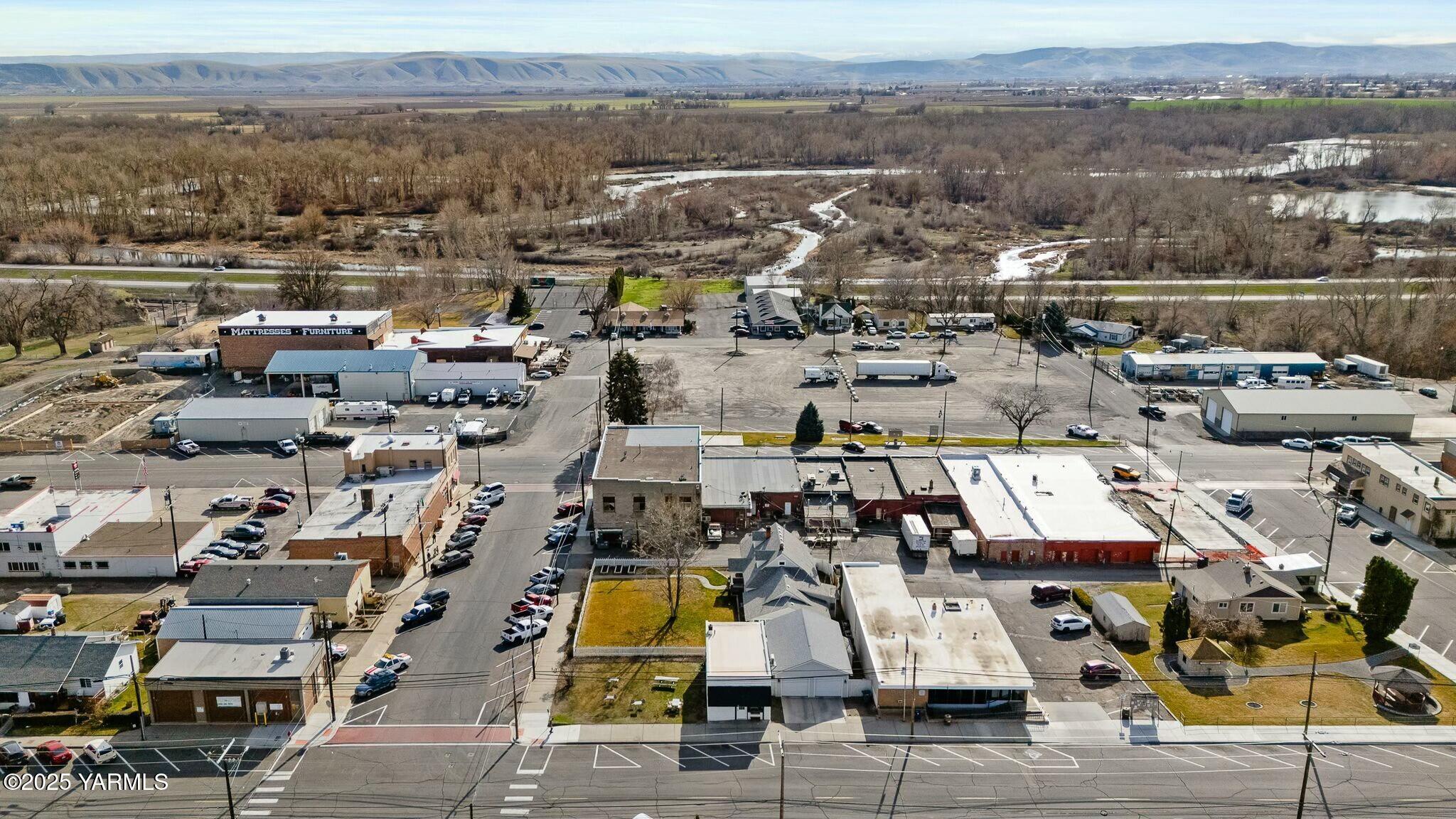 Aerial view of a small-town commercial district beside a winding river, with distant hills.
