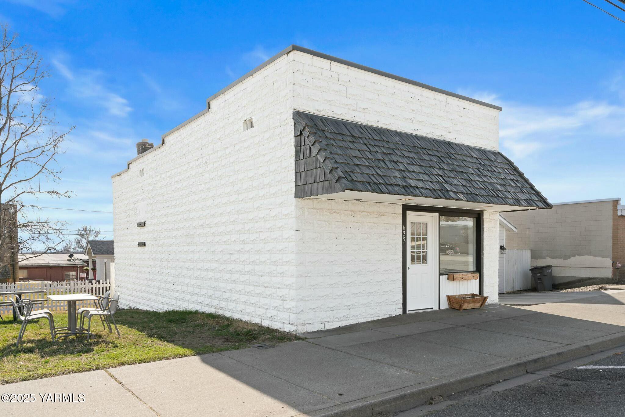 White masonry storefront with a dark shingled awning and outdoor table seating.