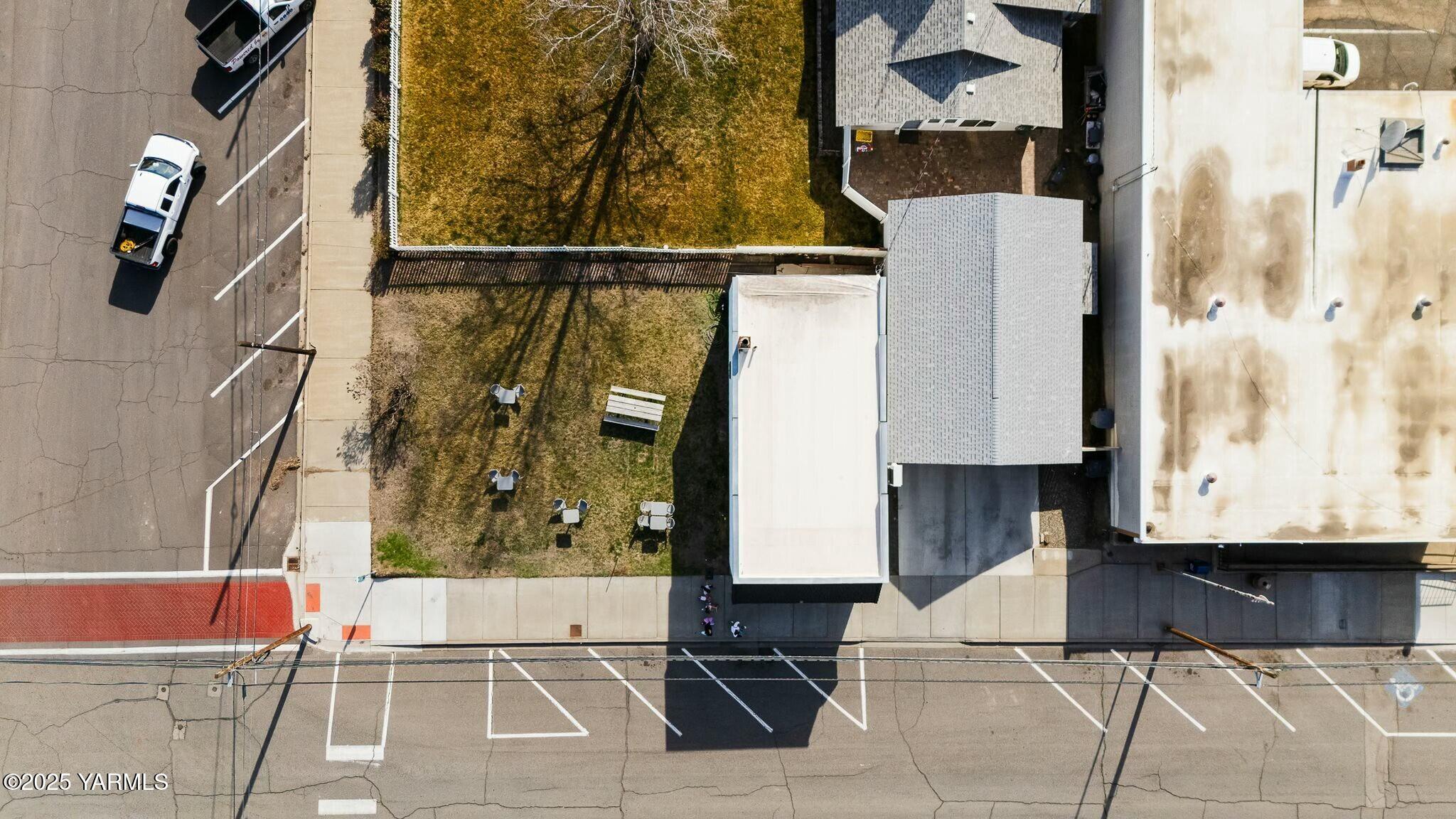 Aerial view of the property, with a fenced lawn beside the building and street parking.