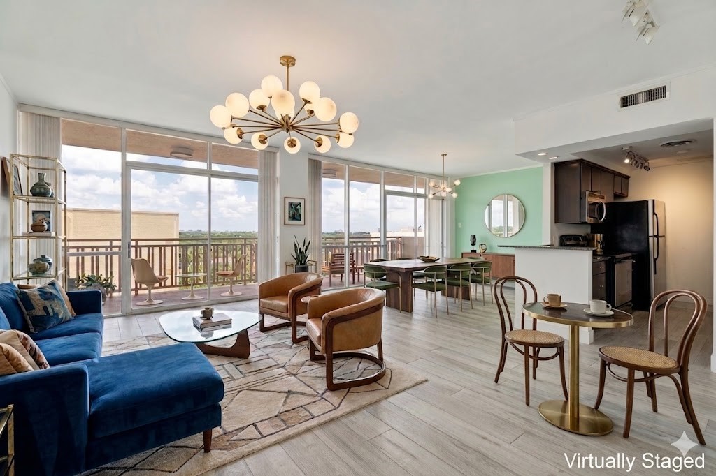 Open-plan living and dining room with blue sectional, brown leather chairs, and floor-to-ceiling balcony windows.