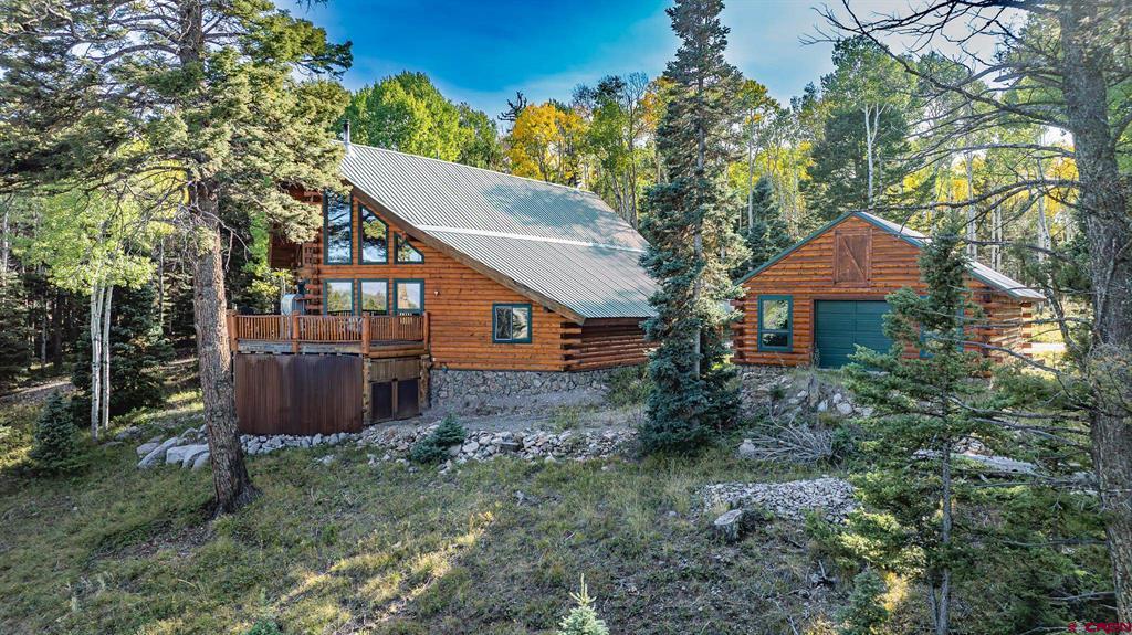 Timber cabin and detached garage nestled among pine trees and rocky terrain.