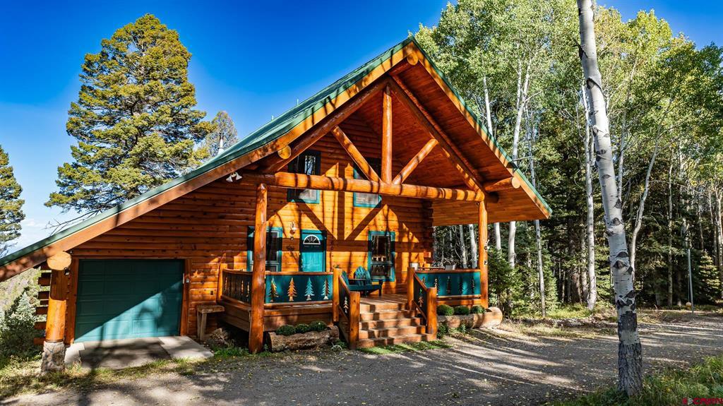 Log cabin with a timber gable, green garage door, and covered porch among trees.