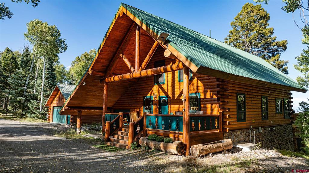 Log cabin with a green metal roof, covered porch, and stone foundation among trees.