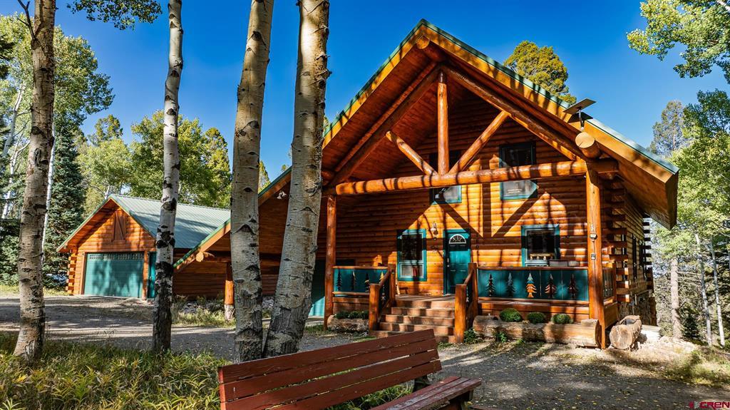 Log cabin with a covered porch and detached garage among aspen trees.