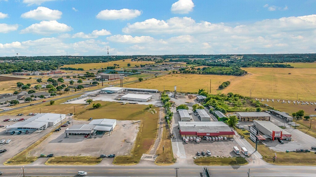 Aerial view of highway-front commercial buildings, parking lots, and open fields.