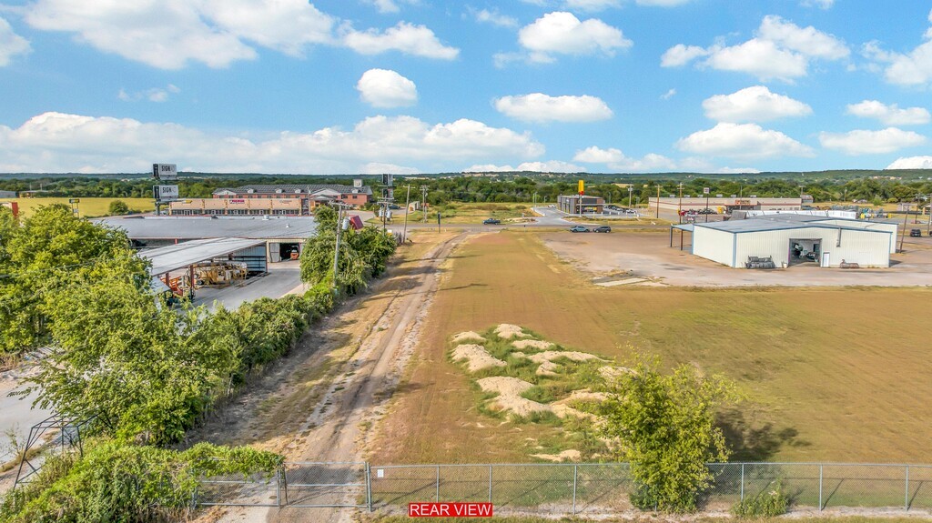 Vacant commercial lot with open grass, a chain-link fence, and neighboring commercial buildings.