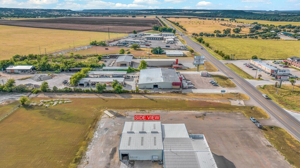 Aerial view of commercial buildings and paved lots beside a highway, surrounded by open fields.