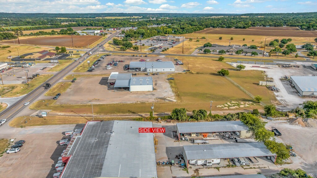 Aerial view of commercial property beside a highway, with open land and metal-roofed buildings.