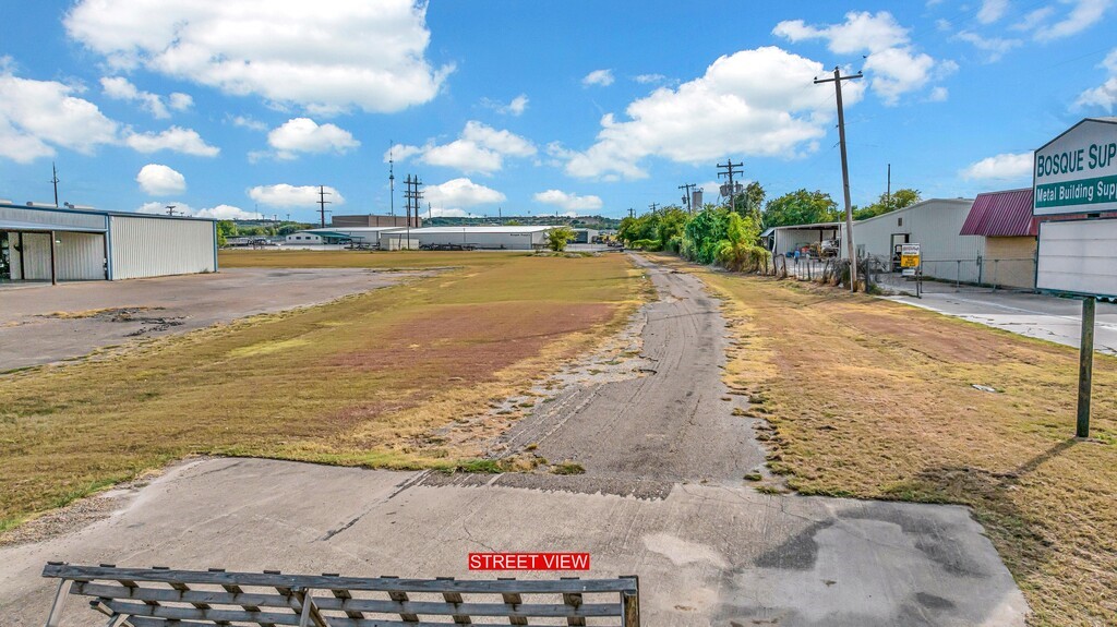 Vacant commercial lot with a paved access lane and neighboring metal buildings.