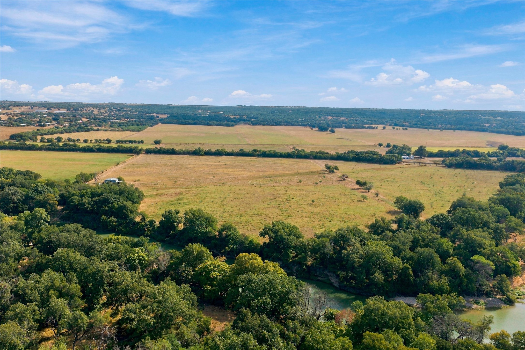 Aerial view of open Texas fields and wooded creek frontage.