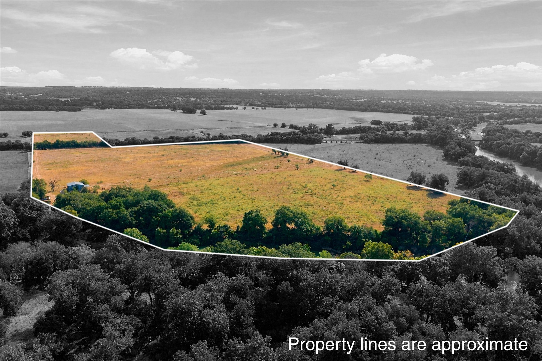 Aerial view of a rural tract outlined in white, with open grassland, trees, and a small outbuilding.