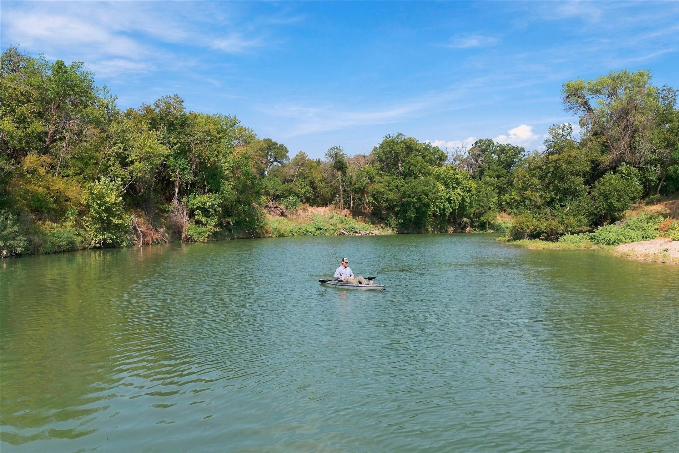 Wooded pond with a person kayaking near the center.