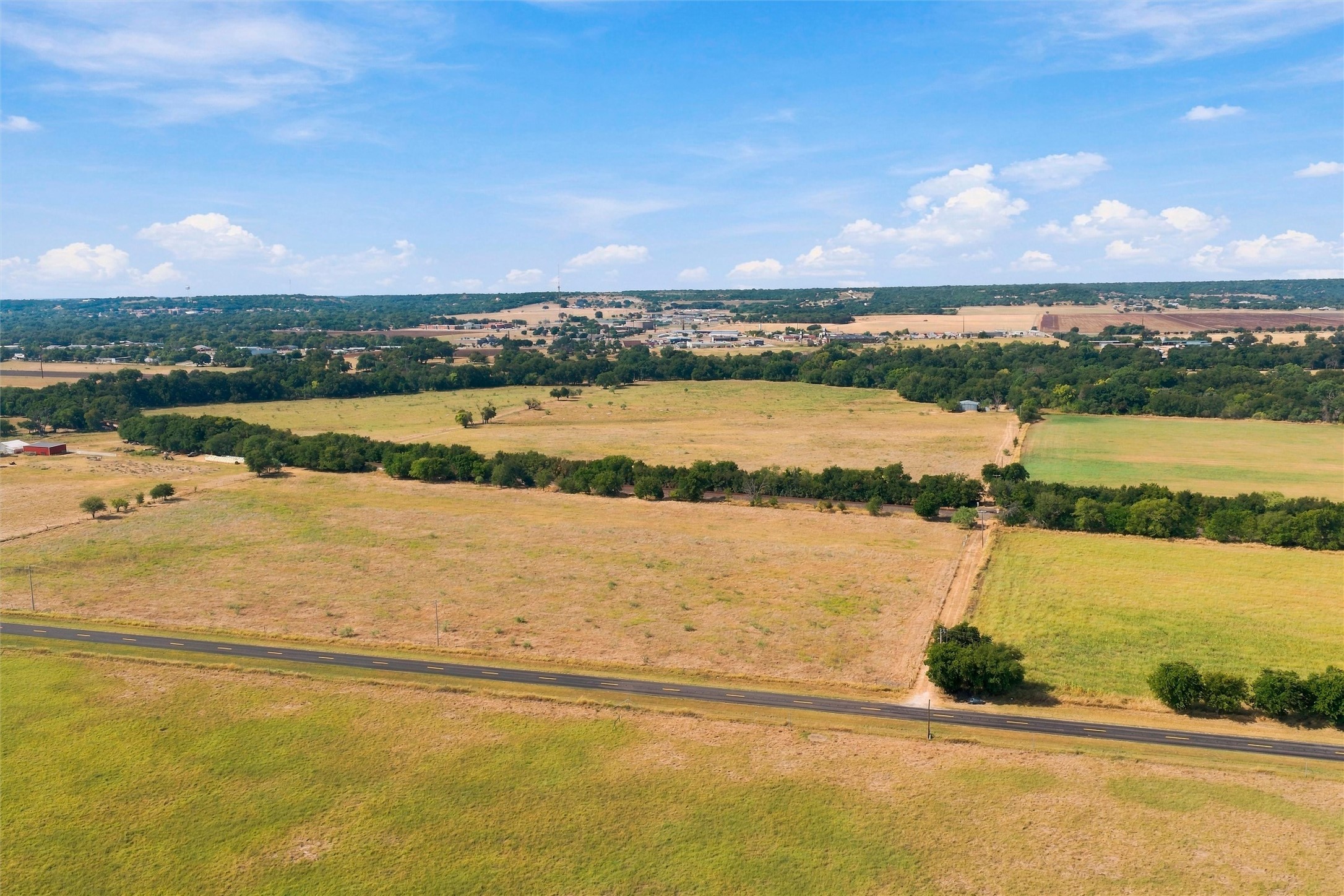 Aerial view of rural acreage with road frontage, pasture fields, and tree-lined boundaries.