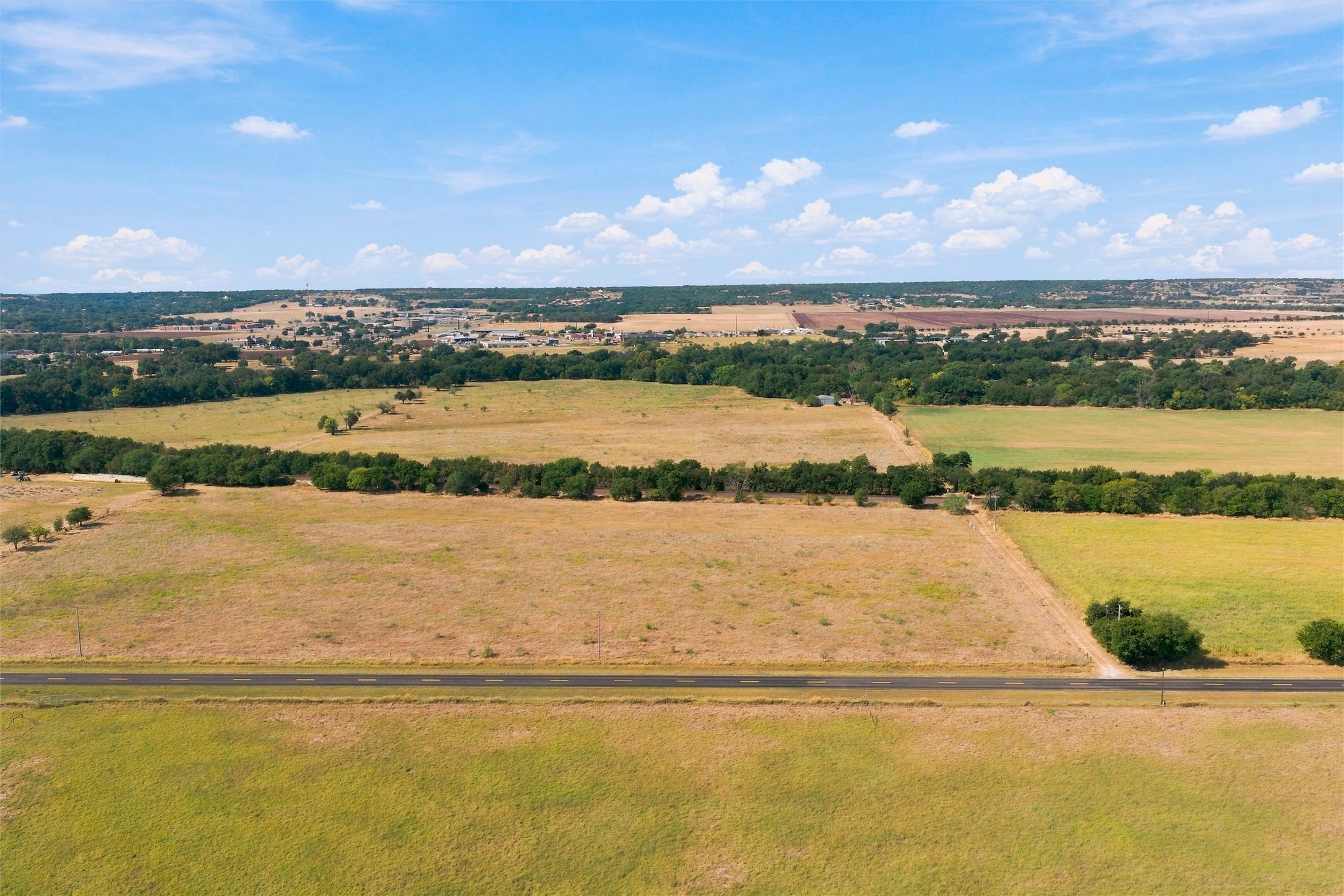 Aerial view of rural pastureland with tree lines and paved road frontage.