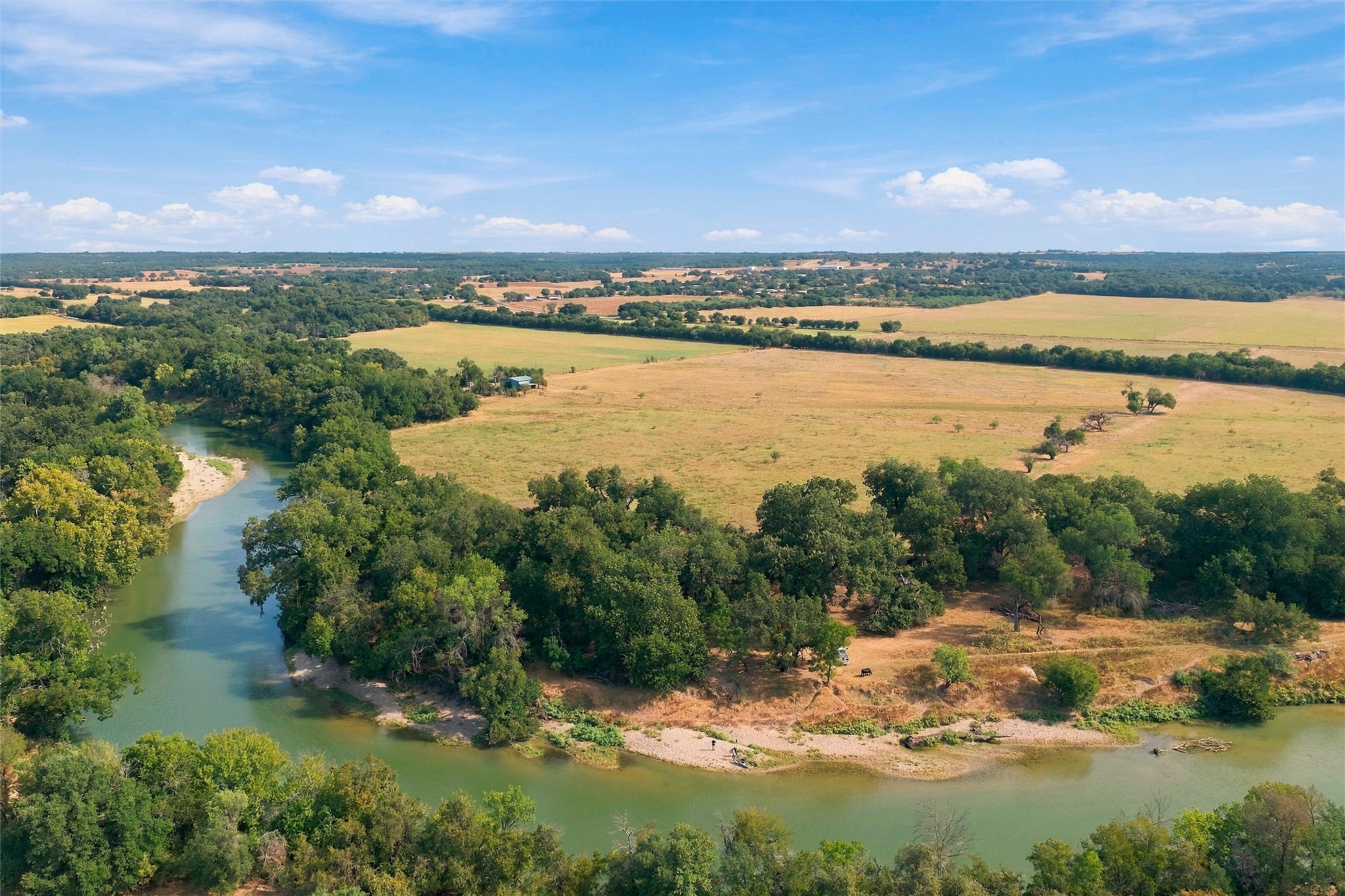 Aerial view of open pasture and wooded land bordering a winding river.