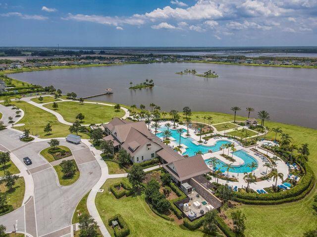 Aerial view of a lakeside community with a clubhouse, several pools, and palm-lined grounds.